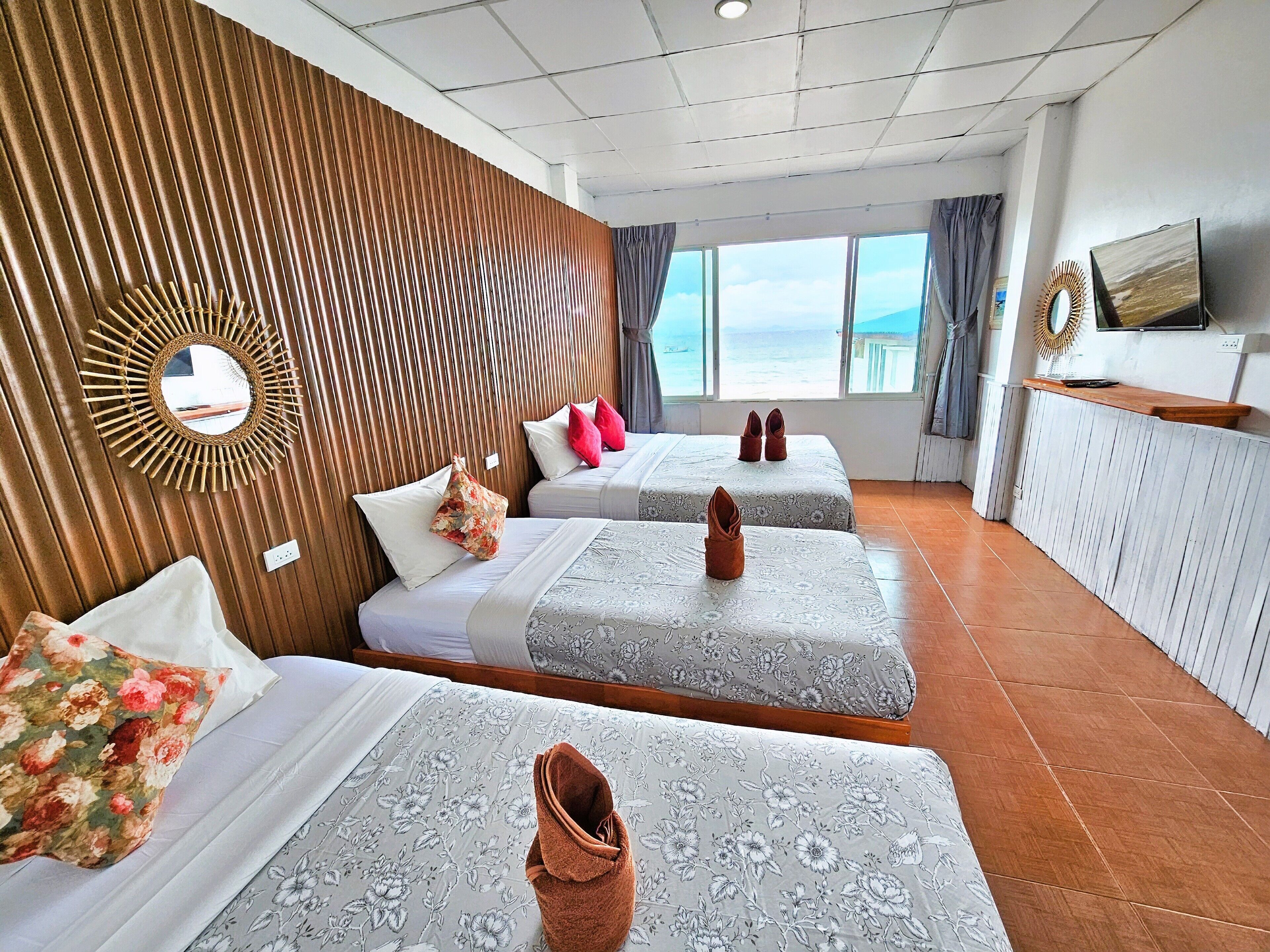 A hotel room with two beds, a wooden wall panel, a large window with a view, a mirror, and a TV on the wall.