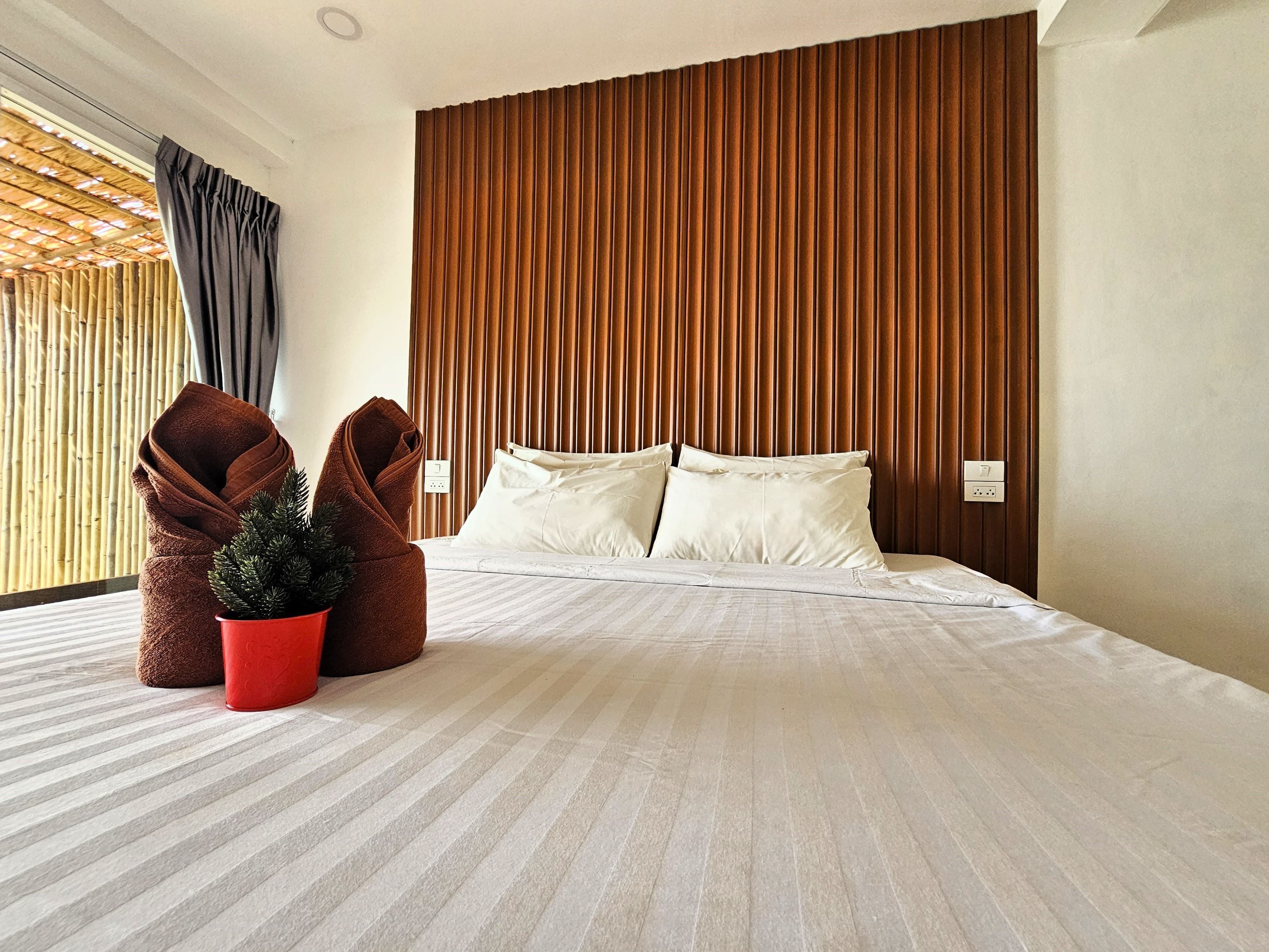 A modern hotel room with a large bed, wooden panel headboard, and a potted plant.