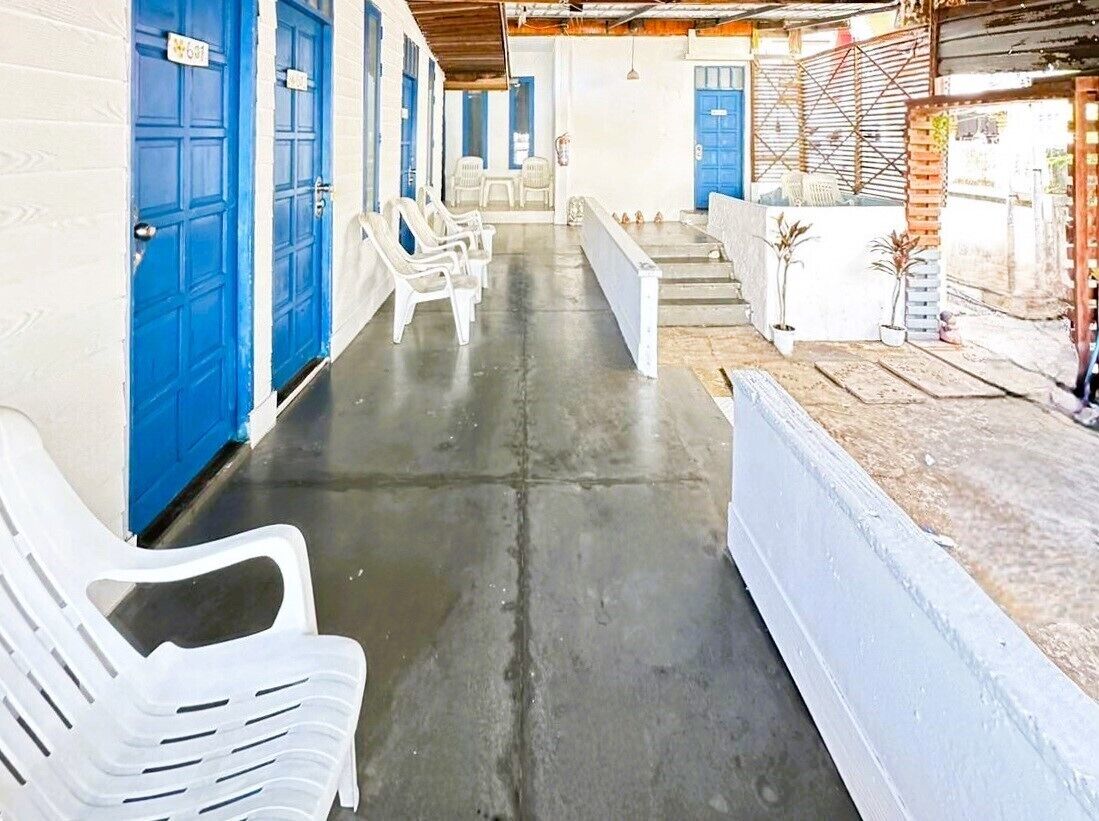A corridor with blue doors, white plastic chairs, and a concrete floor.