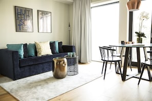 A modern living room with a dark blue sofa, patterned cushions, a white rug, a coffee table, and a dining area with chairs and a vase of flowers. - Frogner House - Vika (Oslo)