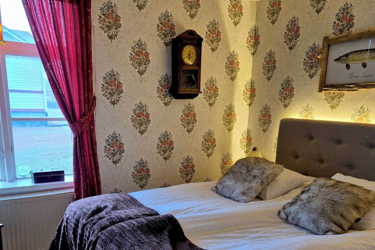 Un dormitorio con cama, un reloj y papel tapiz con motivos florales.