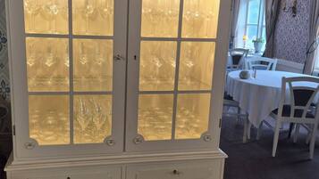 Un mueble blanco y ornamentado con puertas de cristal y cajones, ubicado en una habitación con comedor y papel tapiz estampado.