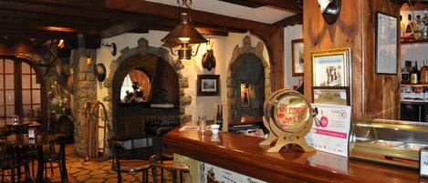 A rustic interior with stone walls, wooden beams, a bar area with stools, and a fireplace.