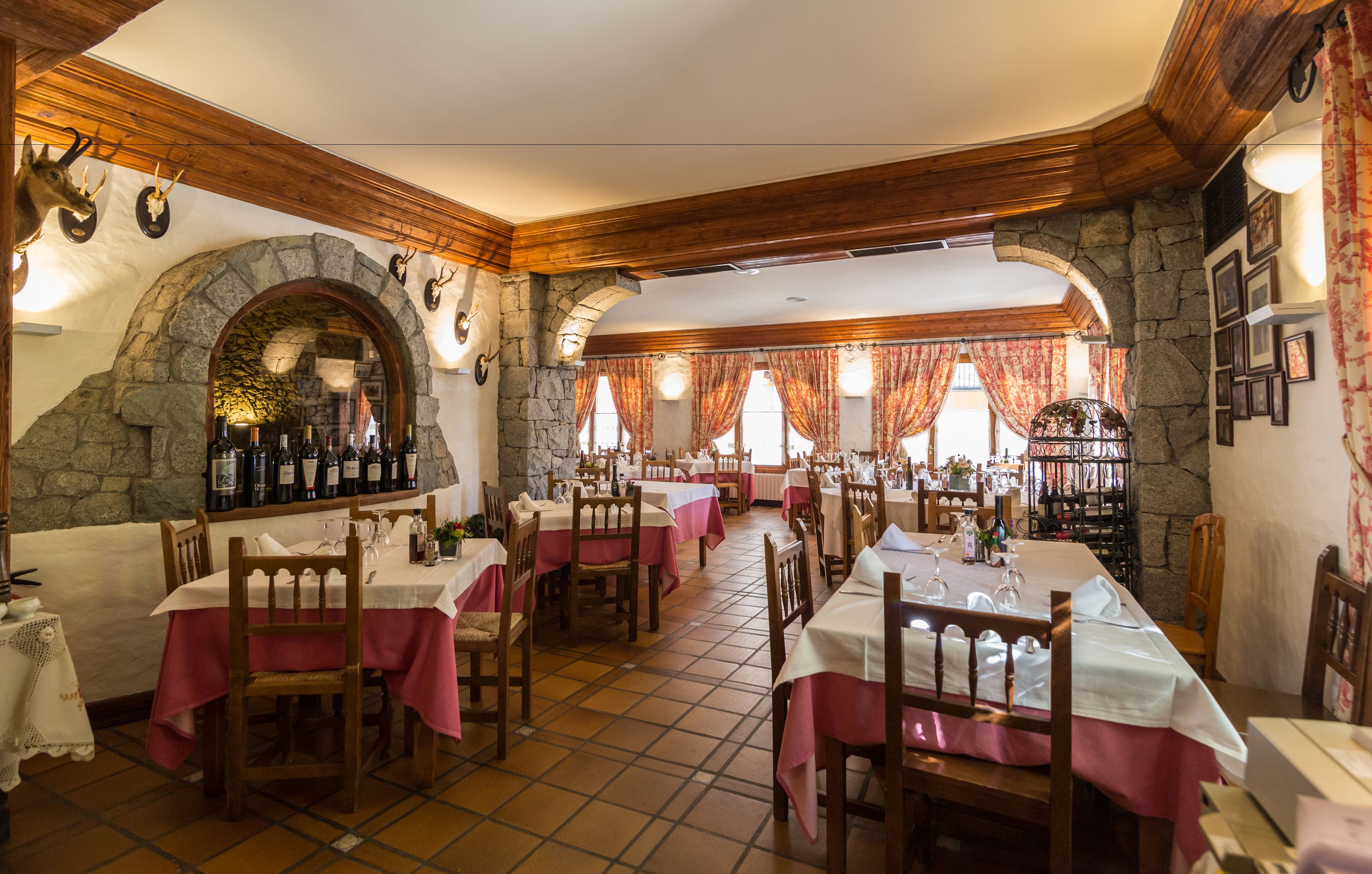 Un restaurant amb parets de pedra, bigues de fusta i taules cobertes amb camises de taula roses.