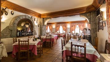 Un restaurant amb parets de pedra, bigues de fusta i taules cobertes amb camises de taula roses.