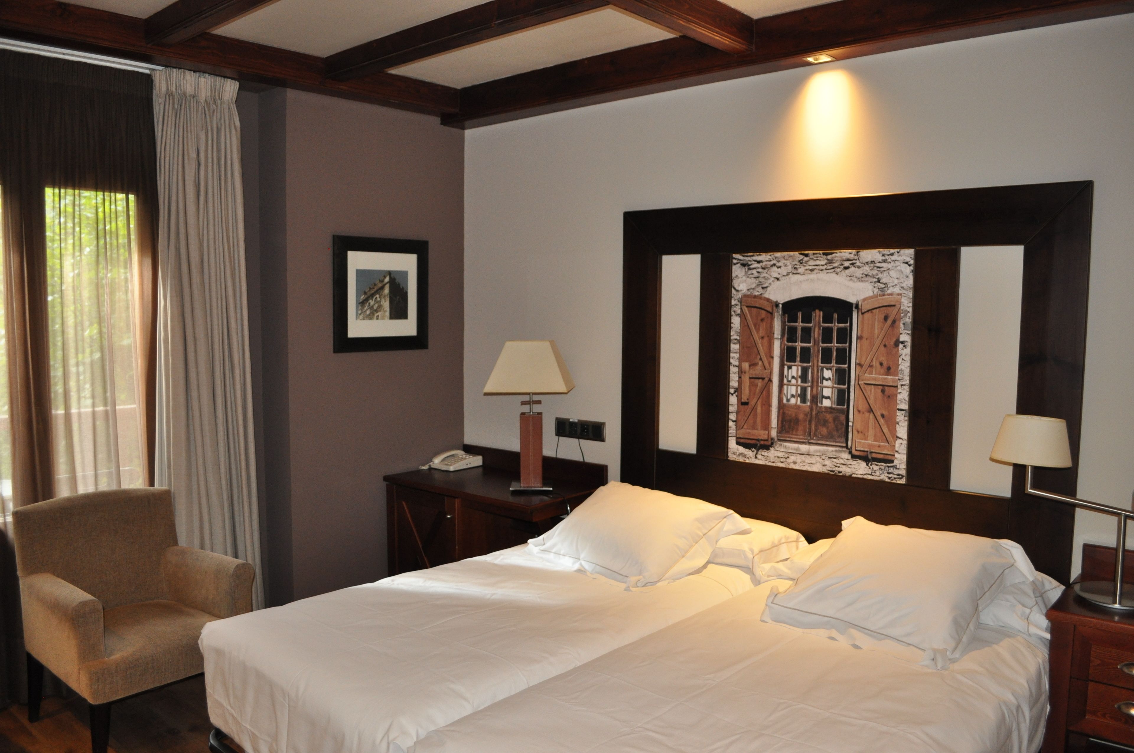 A hotel room with a bed, a chair, a desk with a lamp, and a painting on the wall.