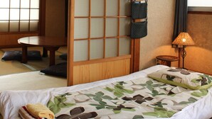 Una habitación japonesa tradicional con suelo de tatami, una cama baja de madera con colcha estampada en verde y blanco, una puerta corredera shoji y una pantalla shoji colgante.