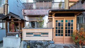 Una casa tradicional japonesa con un portón de madera, escalones de piedra y una pequeña estructura similar a un santuario.