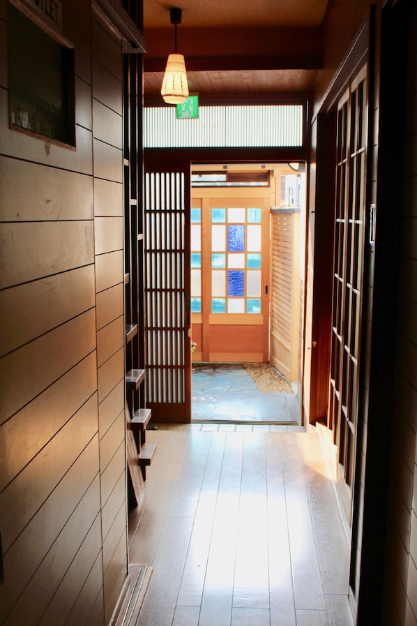 A hallway with wooden paneling, a wooden door with glass panels, and a hanging light fixture. - Jizo House (Kyoto)