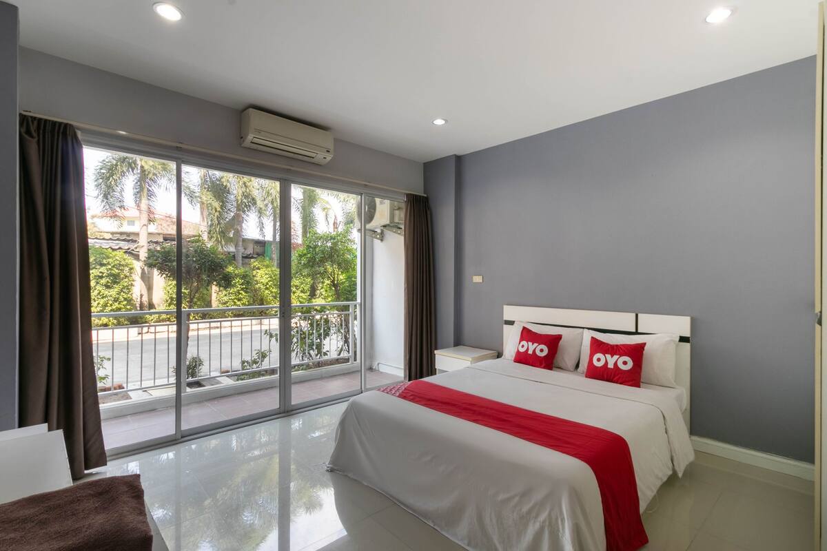 A modern hotel room with a large bed, a balcony with a view of the street, and an air conditioning unit on the wall.