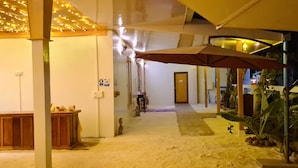 A corridor with a wooden bench, a large umbrella, and a plant area.