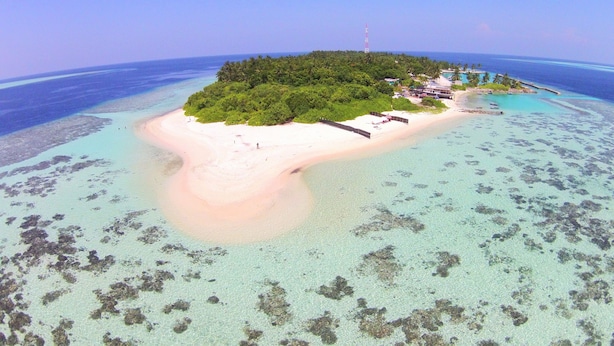 An island with a beach, clear waters, and a small building.