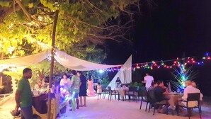 An outdoor dining area with tables and chairs, surrounded by trees and string lights.