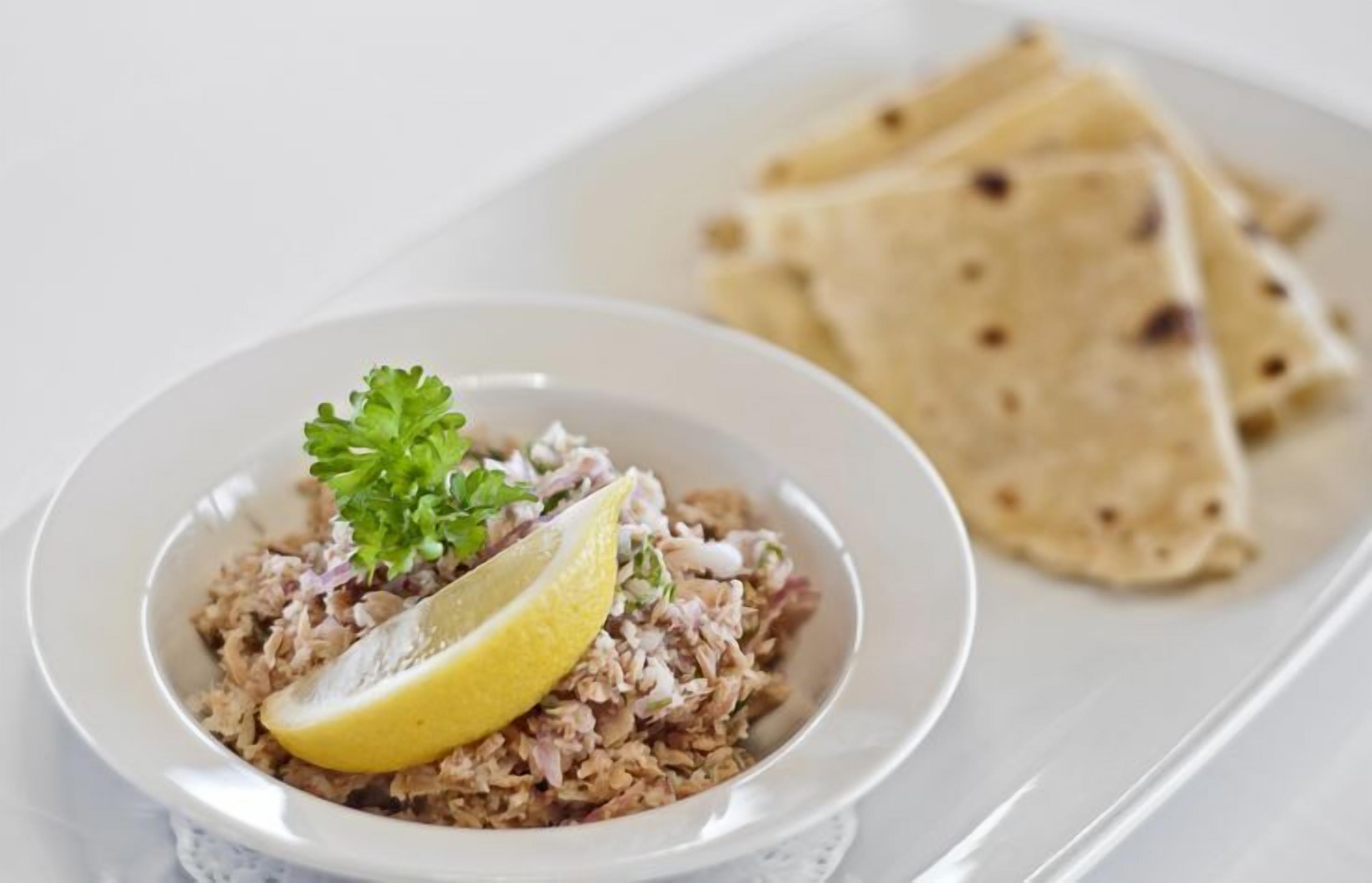 A bowl of rice salad with lemon and parsley garnish, accompanied by flatbreads on a white plate.