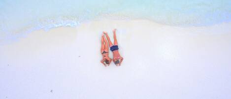 Two people lying on a beach with a clear sky above.