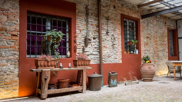 A rustic stone building with a wooden table holding terracotta pots and a metal trash bin. - Camere Centro Storico (Canelli)