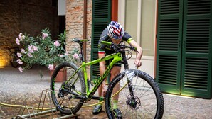 A person washing a bicycle in front of a building with green shutters and a stone wall. - Camere Centro Storico (Canelli)