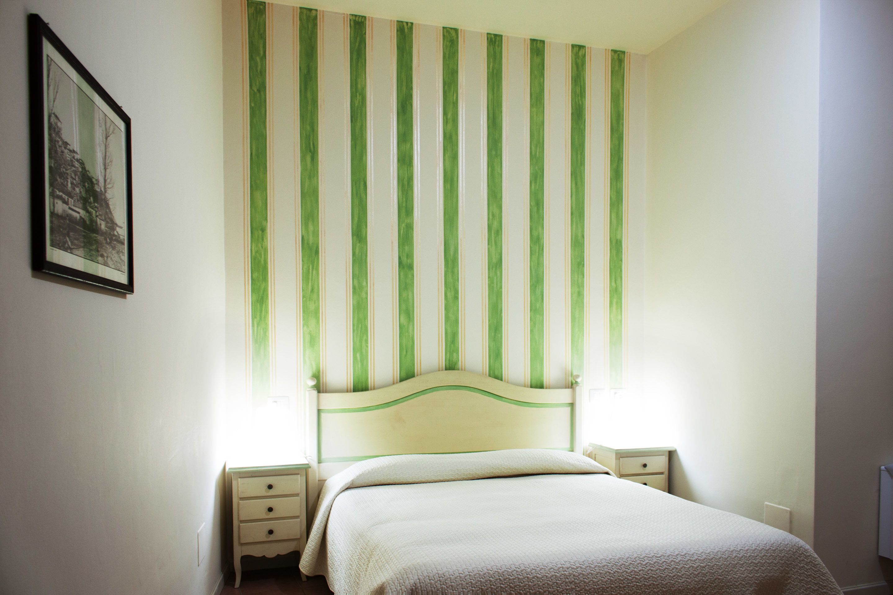 Une chambre à coucher avec un lit, deux tables de chevet, une commode, un tableau encadré au mur et une tête de lit à rayures.