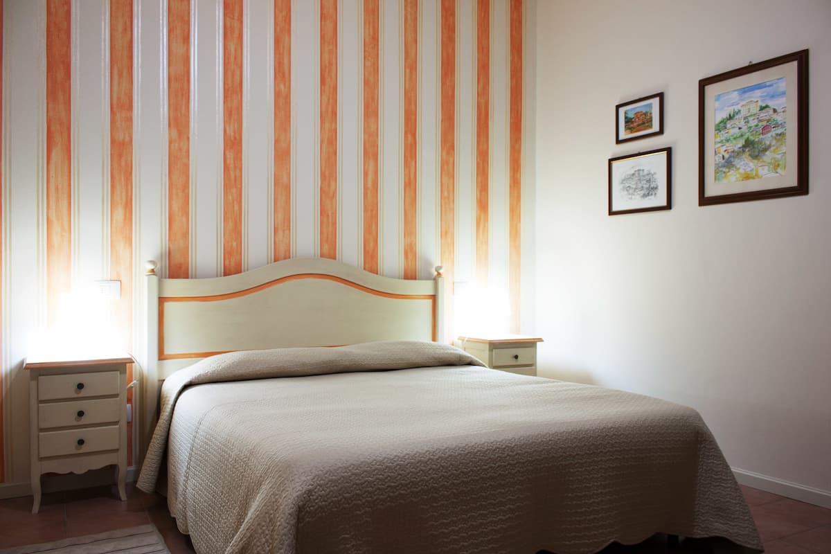 A bedroom with a bed, a nightstand, a drawer, and two framed pictures on the wall.