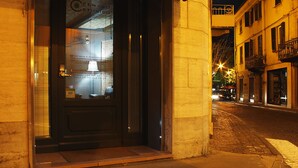 A hotel entrance with a dark door, a glass window displaying a map, and a street view with buildings and lights in the background. - Camere Centro Storico (Canelli)