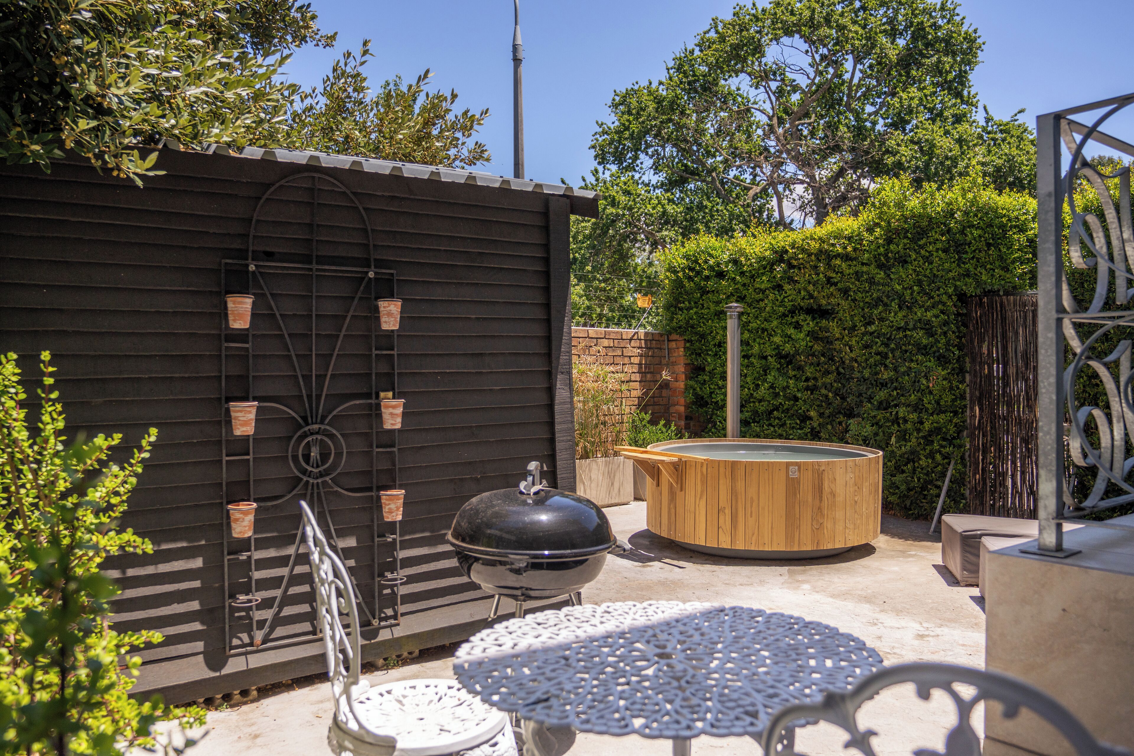 Une terrasse avec un barbecue, un bain à remous en bois et une table ronde.