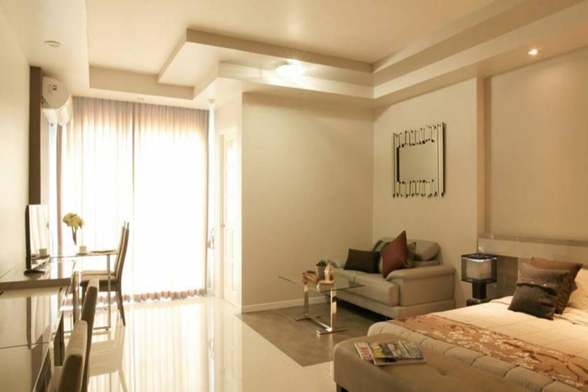 Una habitación de hotel moderna con una cama grande, un sofá, un comedor y un amplio ventanal con cortinas.