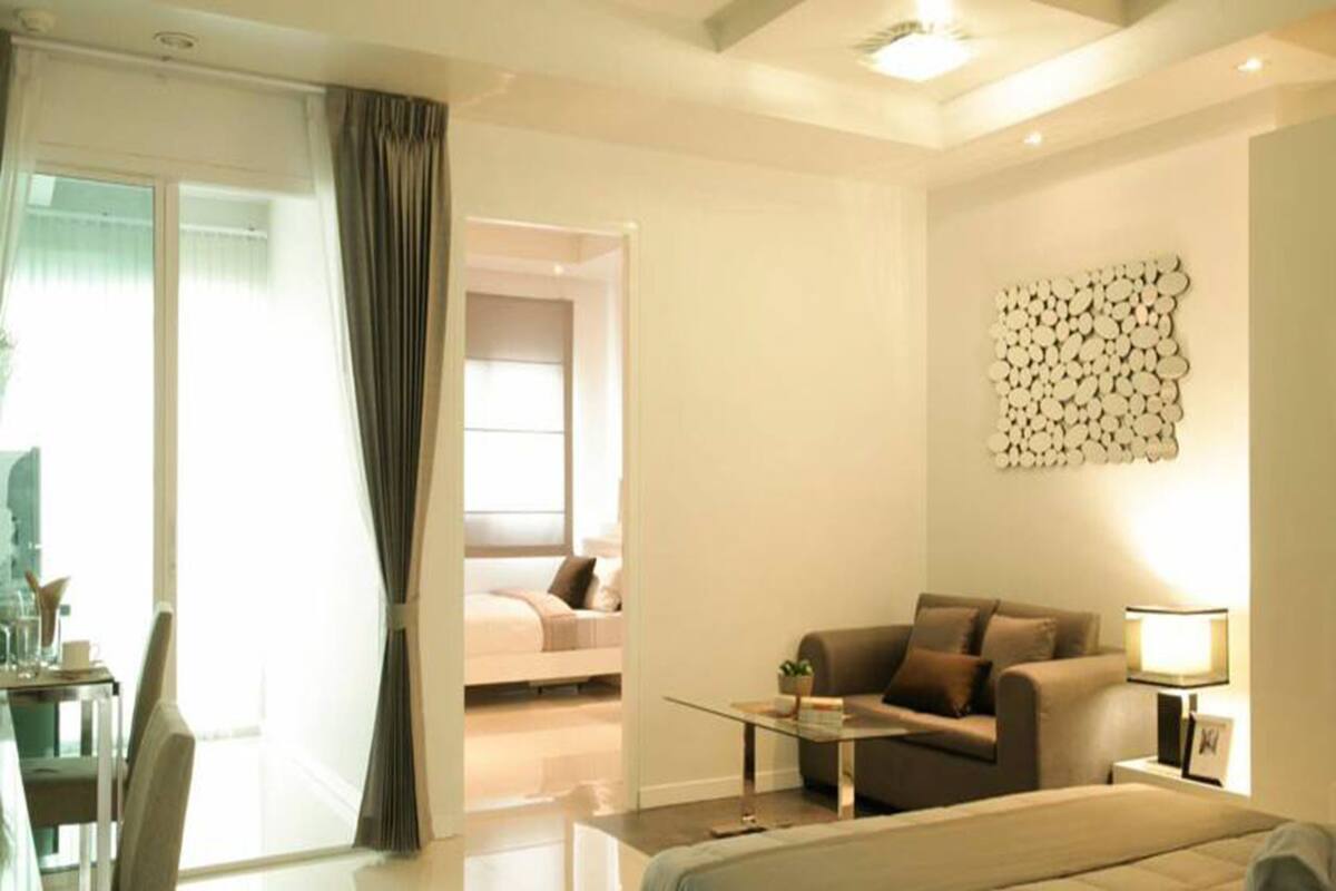 Habitación de hotel moderna con cama, sofá, mesita de café y lámpara. Cuenta con una ventana con cortinas y un adorno en la pared.