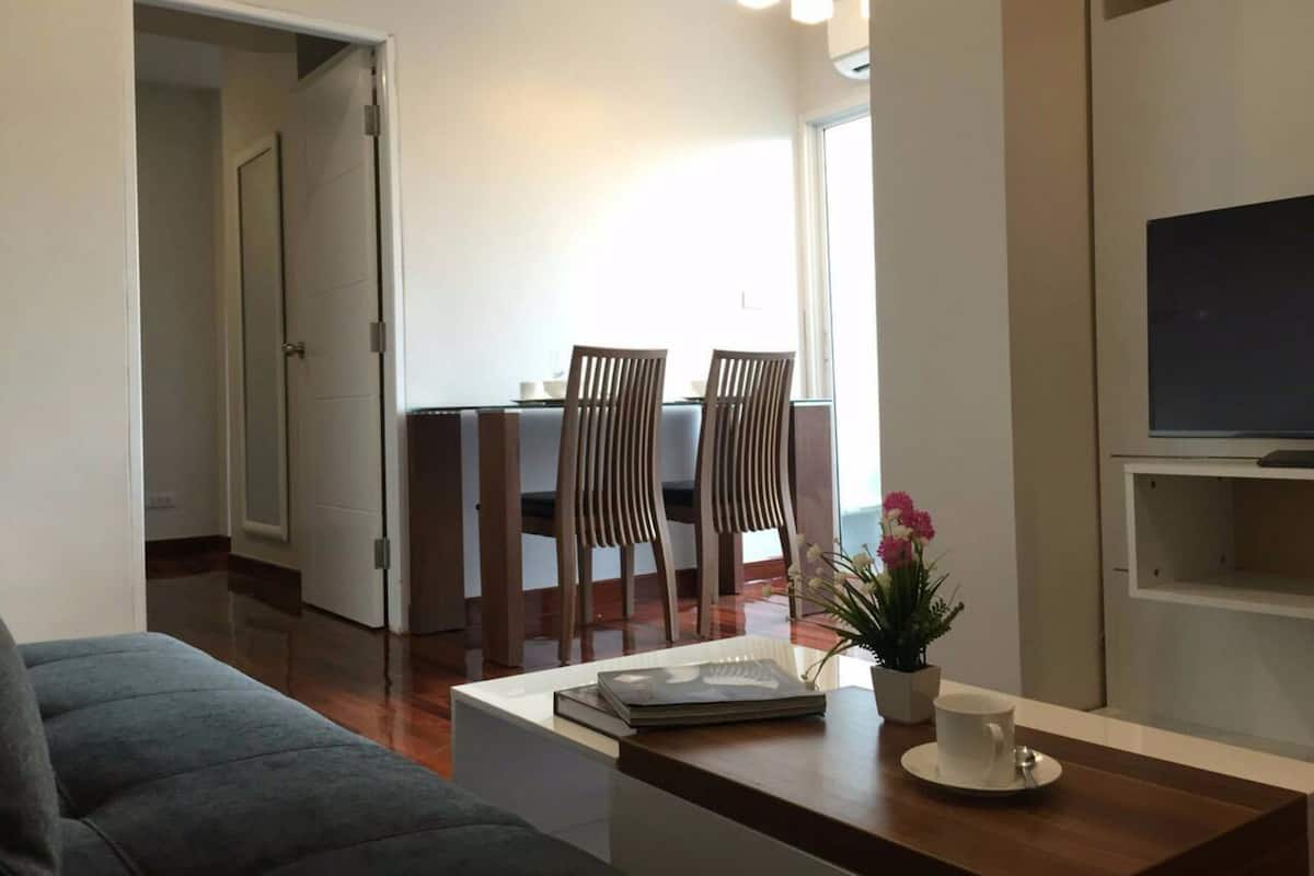 Una sala de estar moderna con sofá, mesa de centro, televisor y comedor con sillas y una mesa.