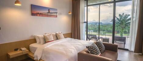 A modern hotel room with a large bed, a sofa, a painting on the wall, and a view of greenery through the window.