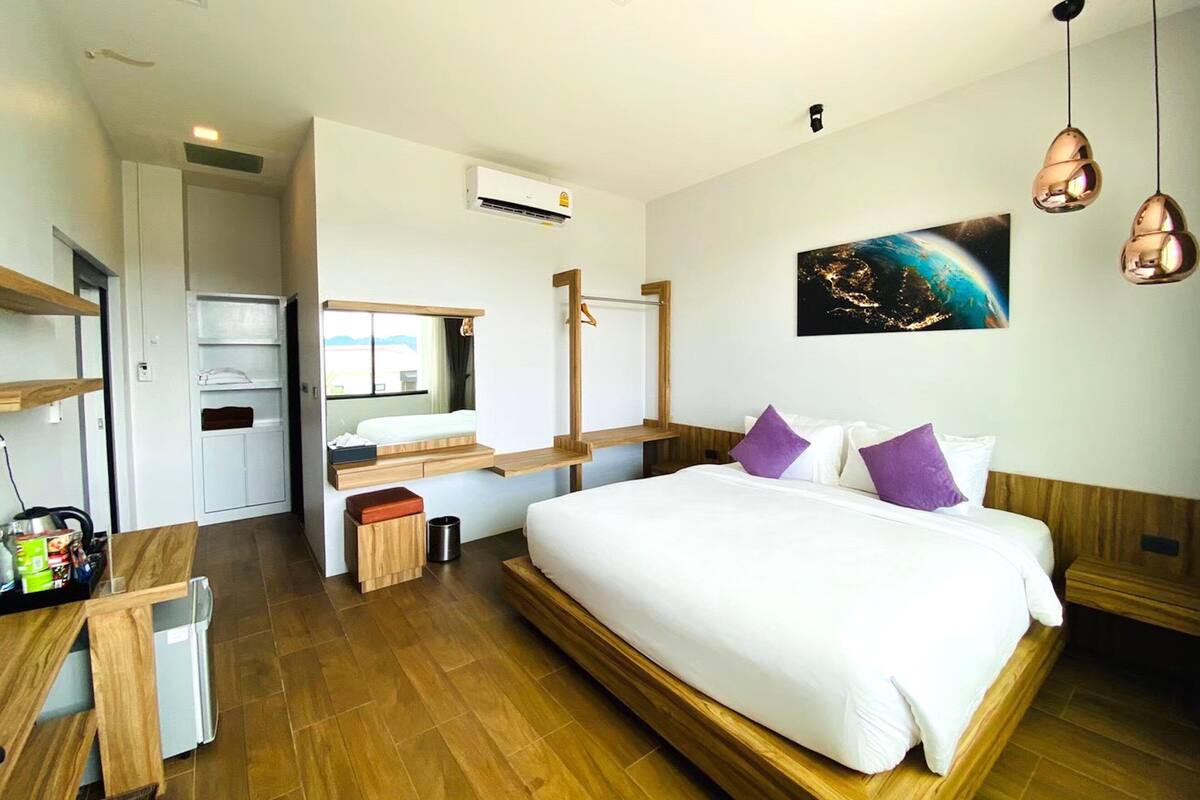 A modern hotel room with a large bed, a desk, a mirror, and a view of the city at night.