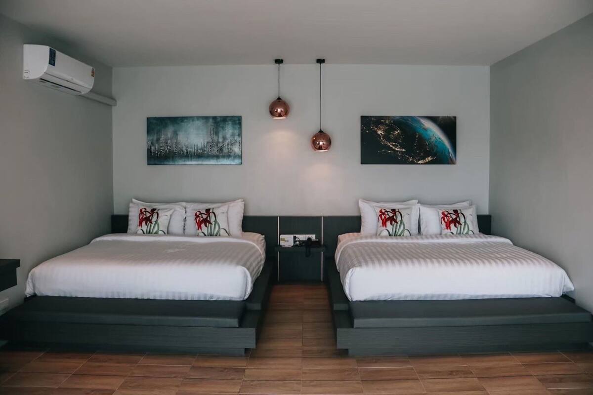 A modern hotel room with two beds, a cityscape painting, a night sky painting, and a pendant light.