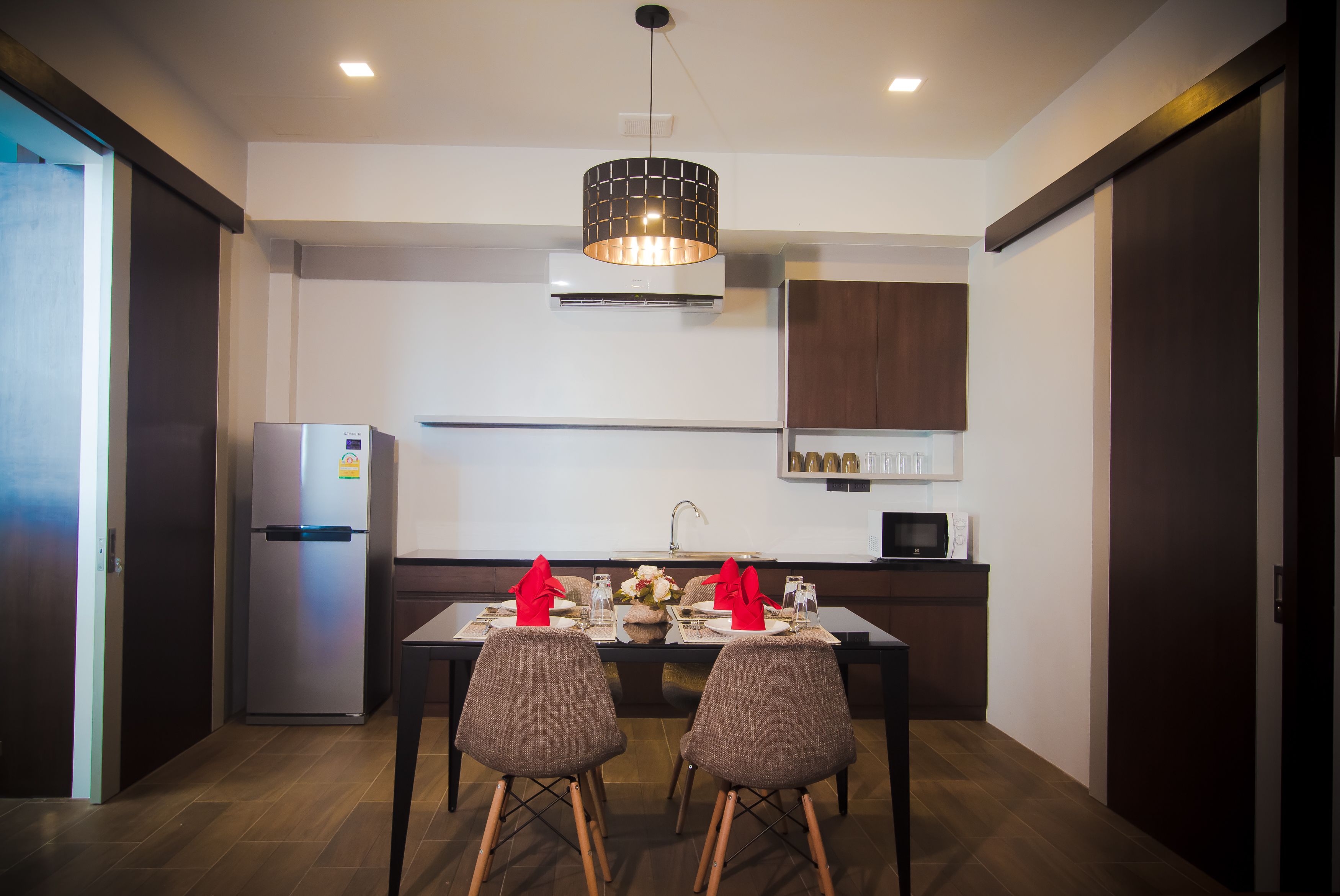 A modern kitchen with a dining area, featuring a refrigerator, microwave, and a hanging light fixture.