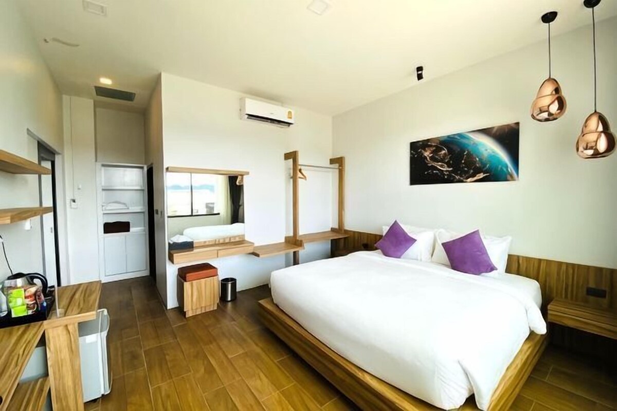 A modern hotel room with a large bed, a desk, a mirror, and a painting on the wall.