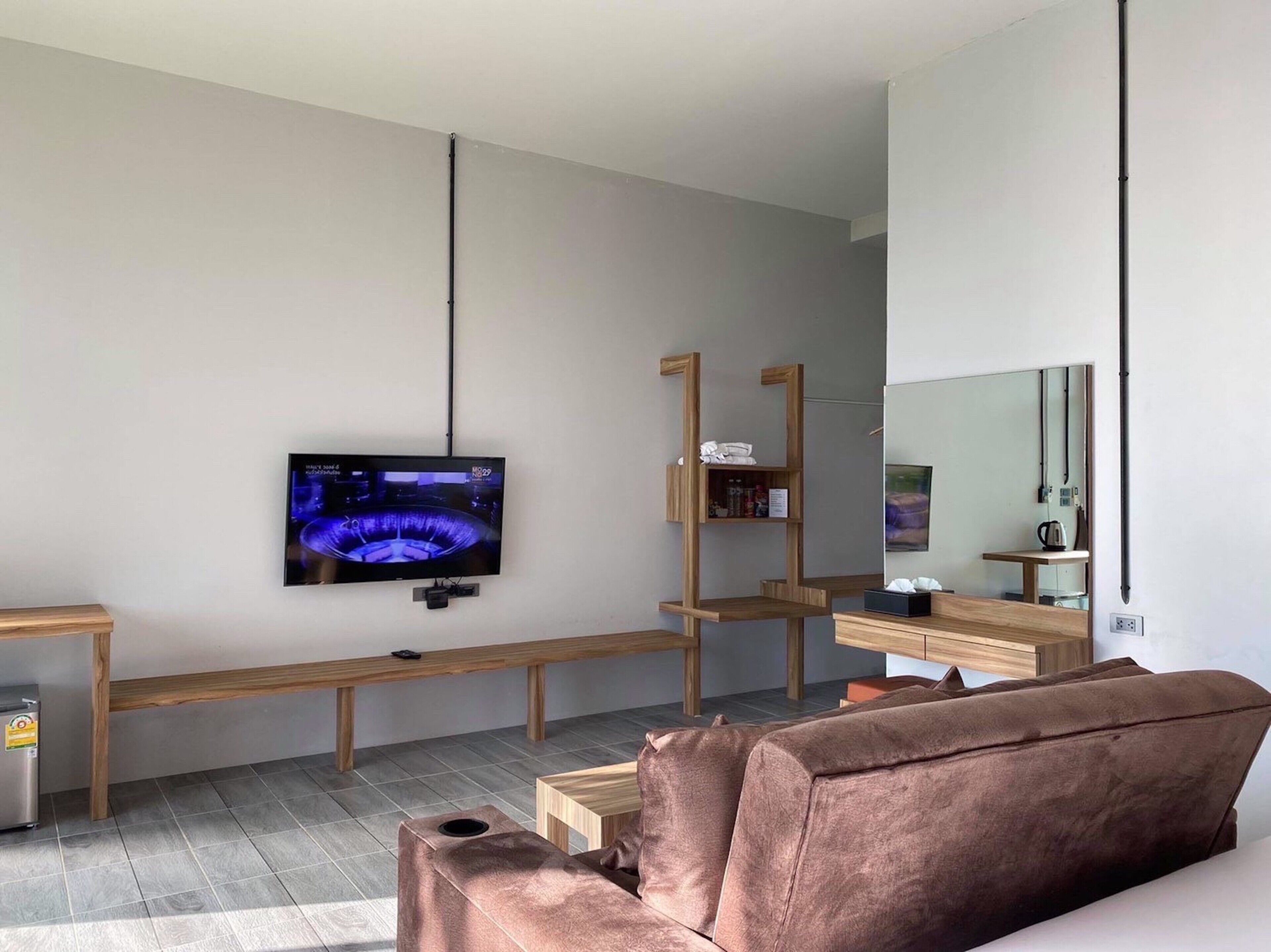 A modern living room with a flat-screen TV mounted on the wall, a wooden bench, a brown sofa, and a small table with a kettle.