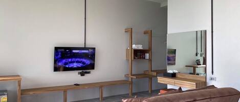 A modern living room with a flat-screen TV mounted on the wall, a wooden bench, a brown sofa, and a small table with a kettle.