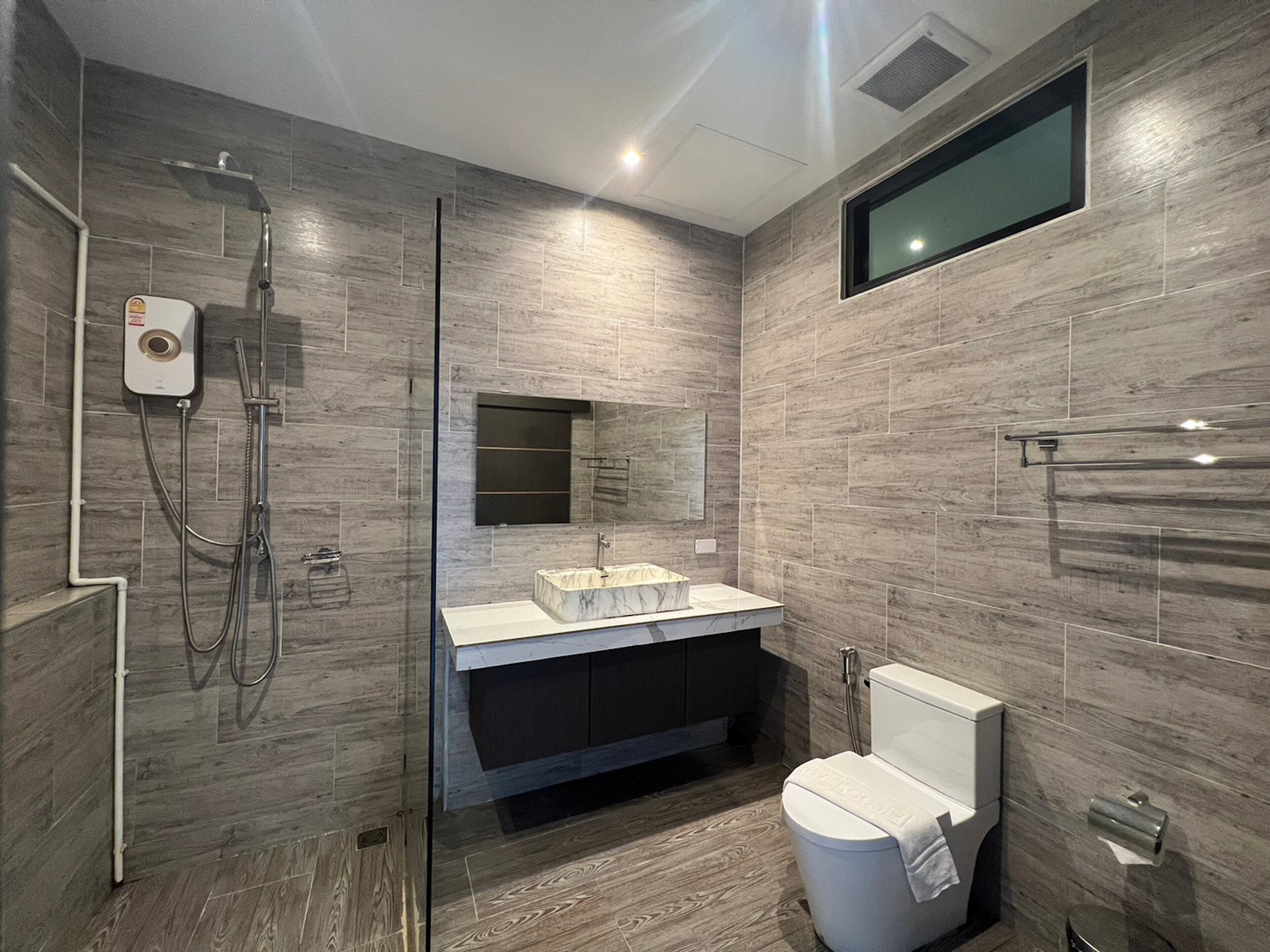 A modern bathroom with a glass-enclosed shower, a marble sink, a dark vanity, and a toilet.