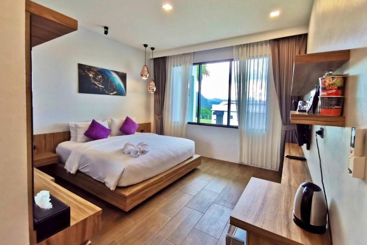 A modern hotel room with a large bed, wooden flooring, a desk, and a view of the outdoors.