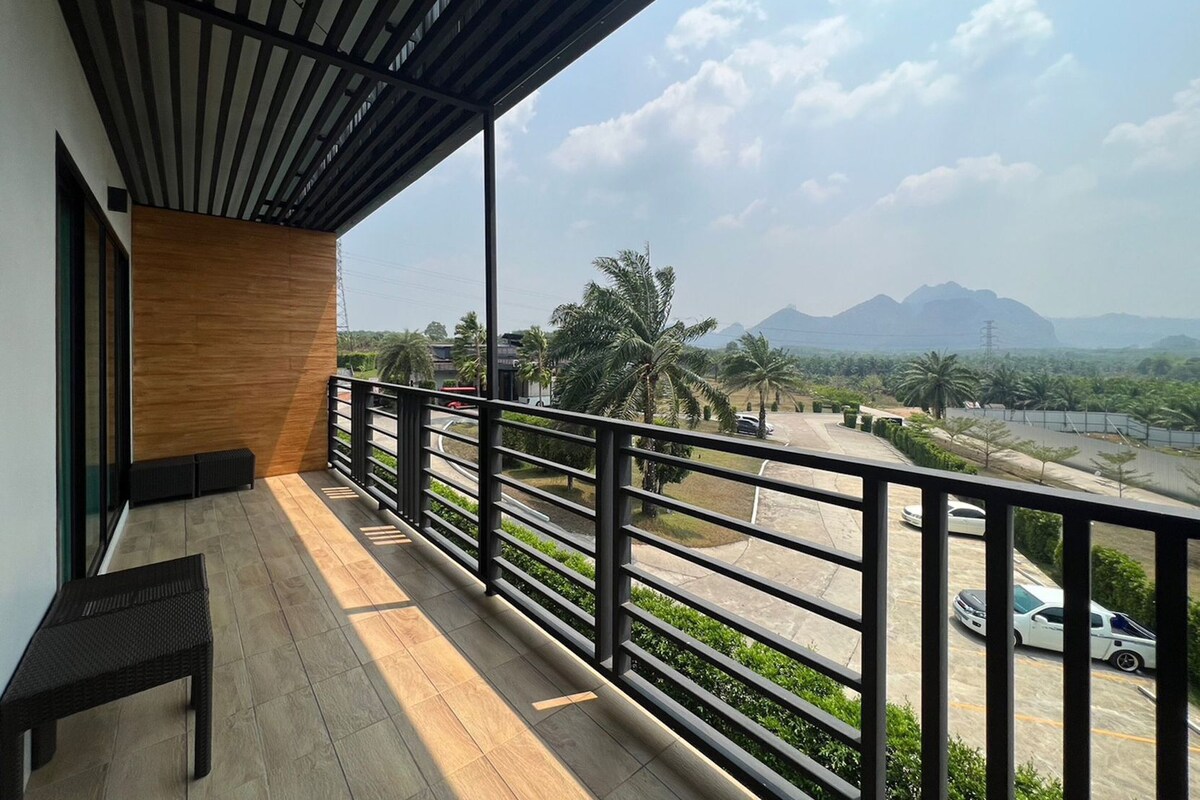 A balcony with a view of a road, palm trees, and distant mountains.