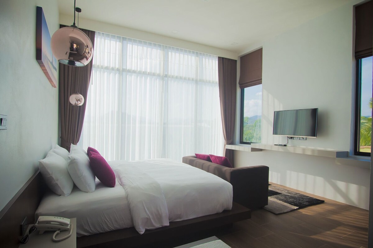 A modern hotel room with a large bed, a flat-screen TV, a phone, and a view of the outdoors.