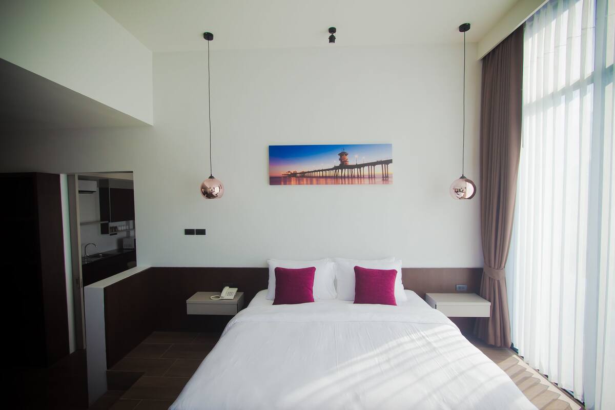 A hotel room with a bed, a nightstand, a desk, a phone, and a painting of a pier on the wall.
