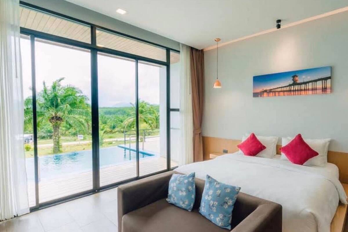 A hotel room with a large bed, a sofa, and a view of a swimming pool and greenery.