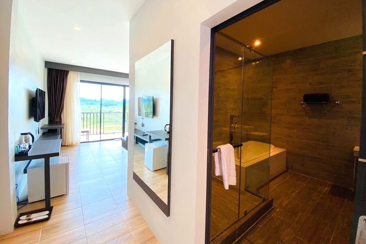 A modern hotel room with a balcony, a glass-enclosed shower, and a flat-screen TV.