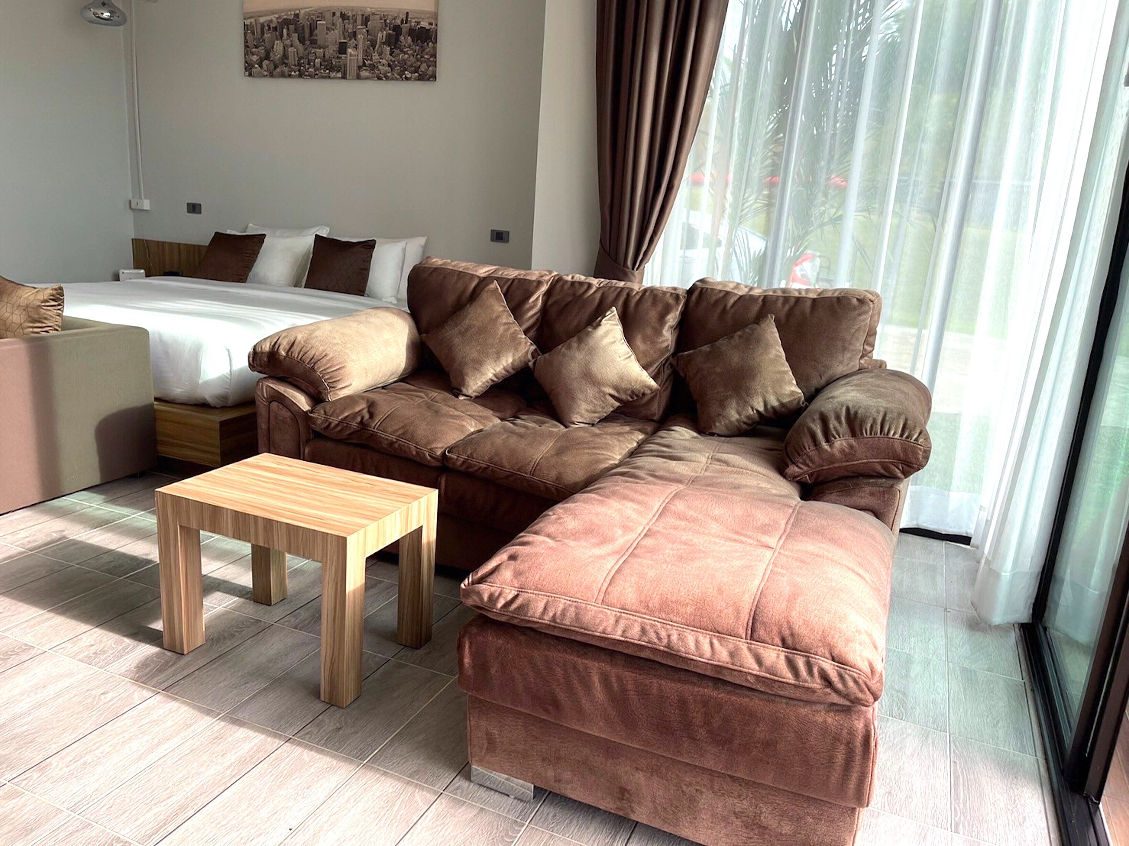 Una sala de estar moderna con un sofá modular, una pequeña mesa de madera y una cama al fondo.