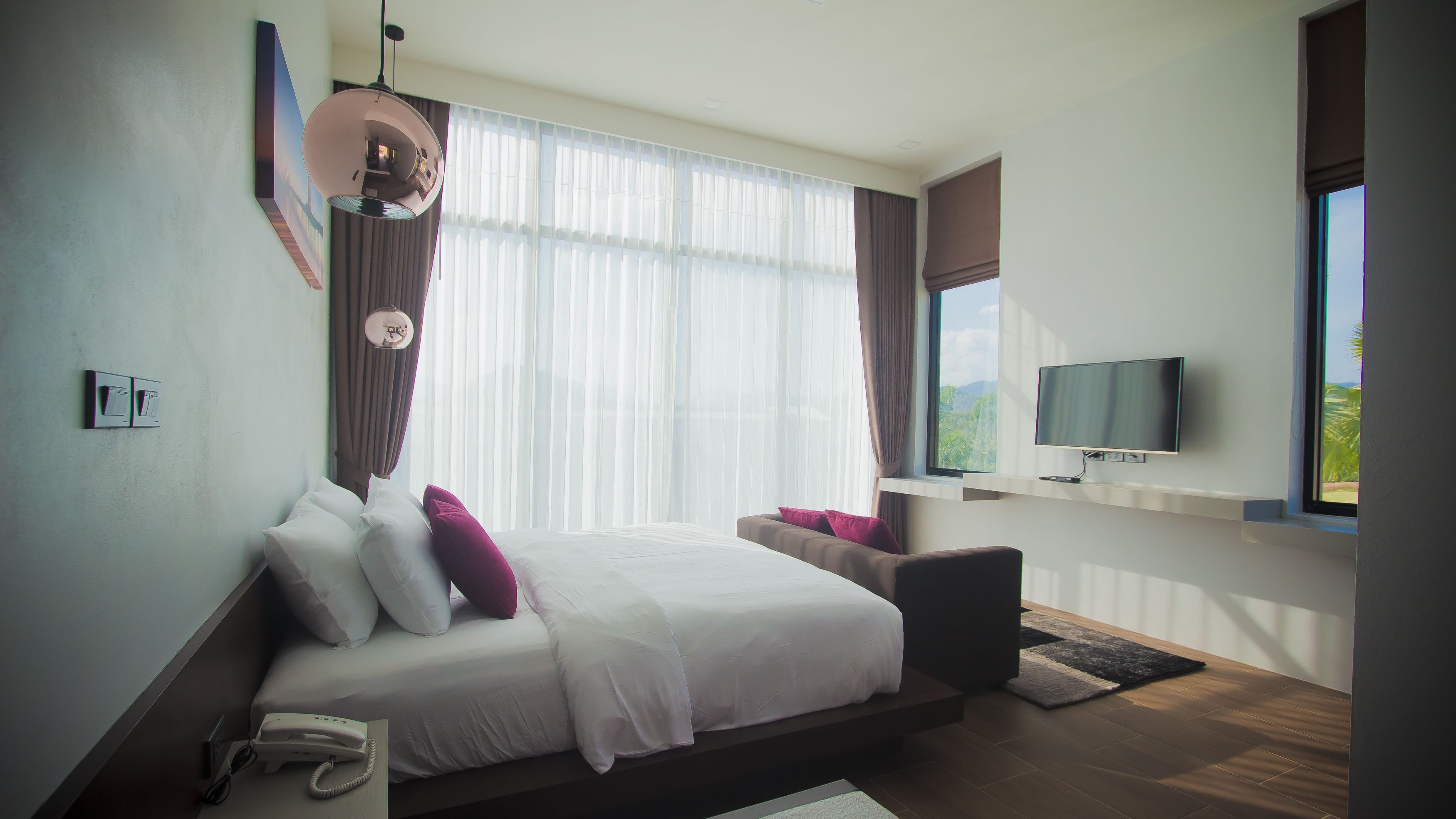 Una habitación de hotel moderna con una cama grande, un televisor montado en la pared y una ventana con vistas a zonas verdes.