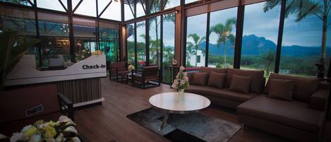 A spacious living area with a check-in counter, a sofa, a coffee table, and a view of palm trees and mountains.