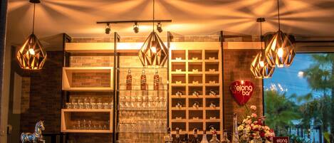 A bar area with shelves of glasses and bottles, a heart-shaped sign, and hanging lights.