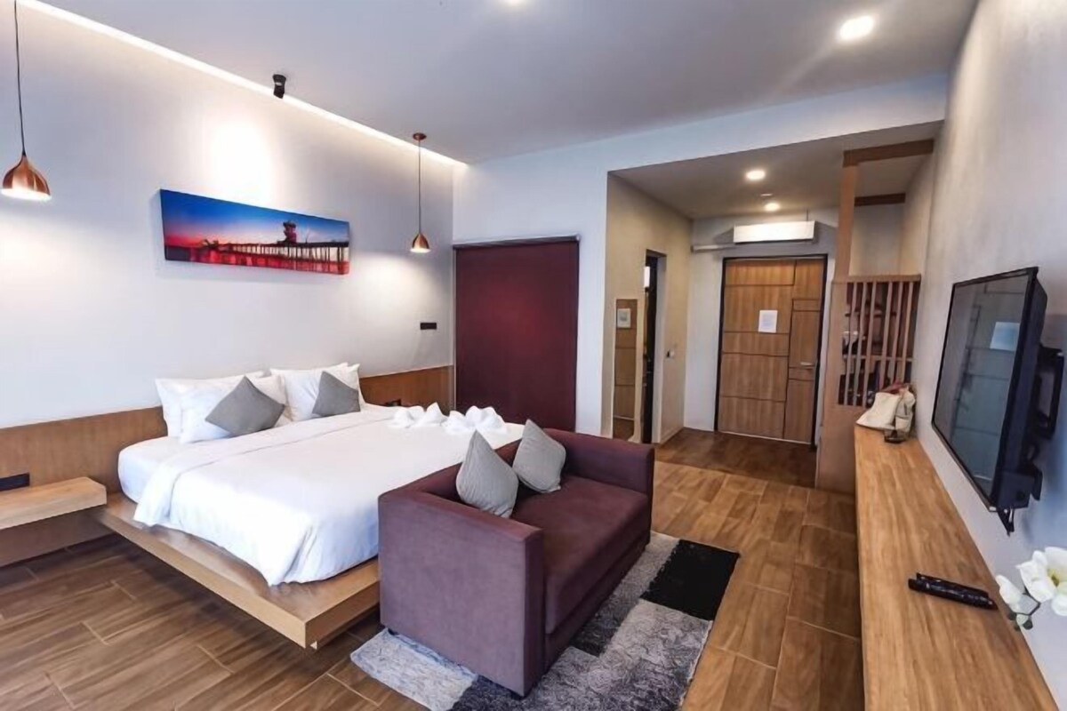 A modern hotel room with a bed, a sofa, a TV, and a wooden floor.