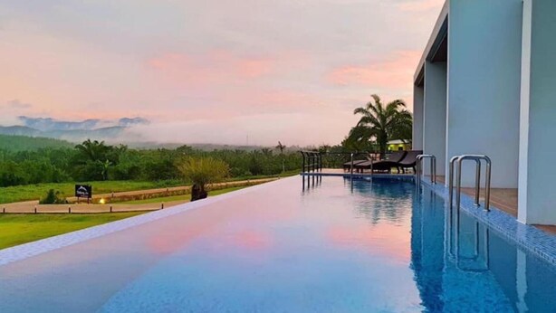A pool with a view of a sunset, a palm tree, and a sign in the background. - Belong Jin The Dam Hotel & Resort (Ban Ta Khun)