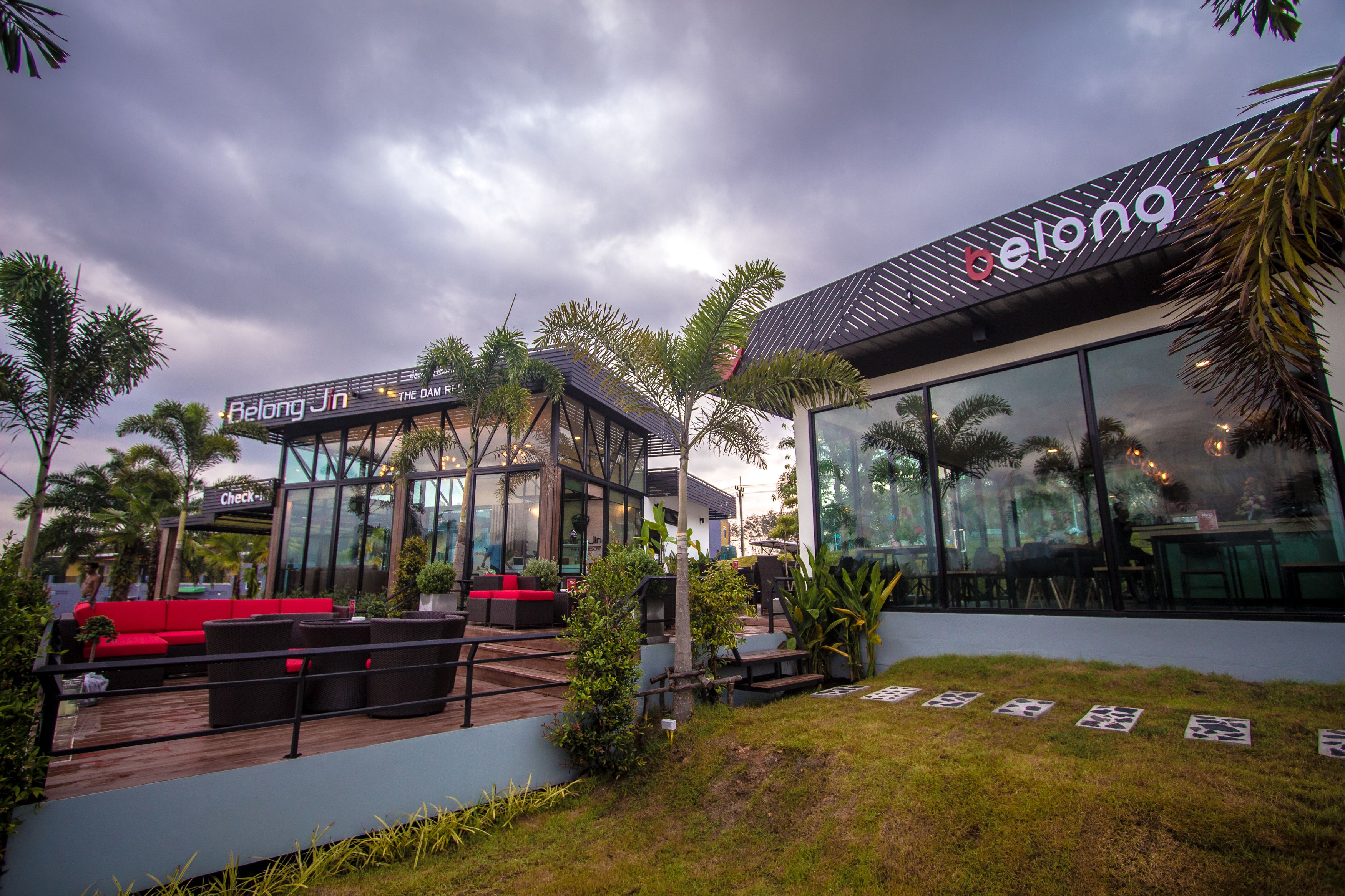 A modern hotel with a glass facade, outdoor seating area, and palm trees.