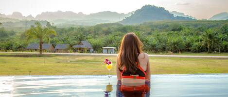 Una mujer en una piscina con vistas a un paisaje tropical y montañas lejanas.